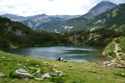 a person sitting in the grass next to a lake at Deluxe Studio 200m from Ski Road in Bansko