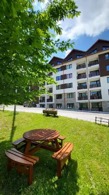 a picnic table and two benches in the grass in front of a building at Premium StudioApartment in Borovets Gardens in Borovets