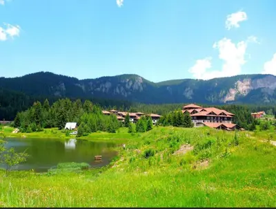 a green field with houses and a river and mountains at Deer Lake 521 at Oak Residence Hotel & Relax in Smolyan