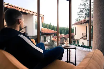 a man sitting in a chair looking out of a large window at Вила Форте Villa Forte in Pamporovo