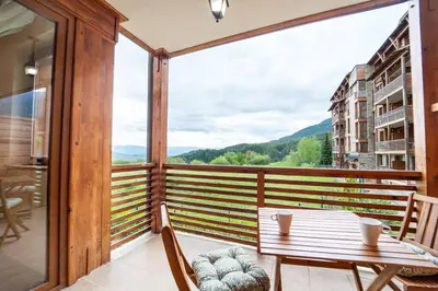a balcony with a table and chairs and a large window at Best Mountain View Chalet in Bansko