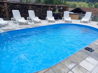 a large blue pool with chairs and a woman standing next to it at Kъща за гости Демария in Koprivshtitsa