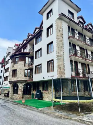 a large white building with a green lawn in front of it at Апартамент Касъл in Pamporovo