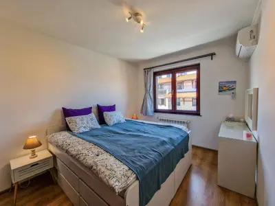 a bedroom with a bed with blue sheets and a window at Pastels - 2BD in Trinity Bansko with underground parking by Flat Mаnager in Bansko
