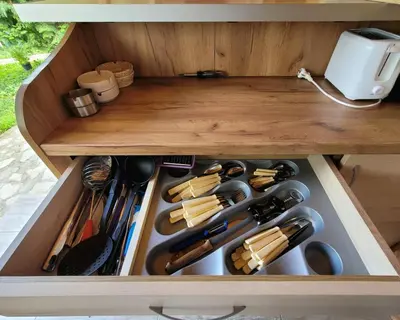 a drawer in a wooden cabinet filled with cooking utensils at Вила Виктория in Chekhlare