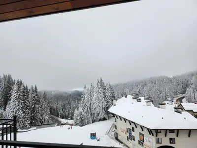 a view from the balcony of a house in the snow at Pine & Wine Bathtub Apartment in Pamporovo