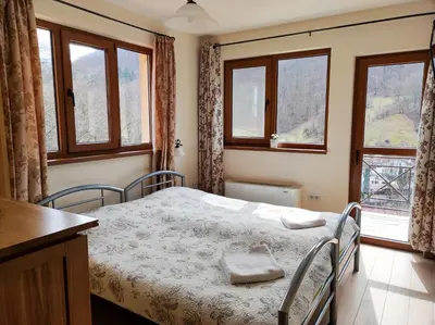 a bedroom with a bed with two chairs and windows at Терасите - Къща 4 in Ribarica