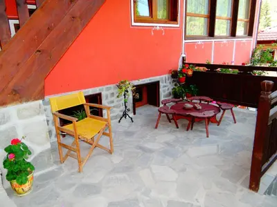 a patio with a table and chairs and a red building at Denis Guest house in Koprivshtitsa