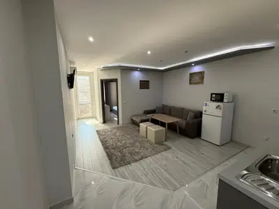 a living room with a couch and a table and a refrigerator at Апартаменти в сърцето на парка in Sandanski