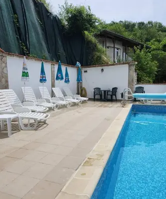 a swimming pool with white chairs and blue umbrellas at Хотел Марио in Melnik
