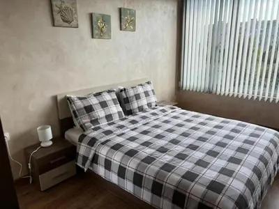 a bedroom with a bed with a checkered blanket and a window at Апартамент Комфорт, близо до Летището in Sofia
