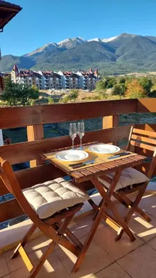 a wooden table and chairs with wine glasses on a balcony at Belvedere Holiday Club - Mountain View in Bansko