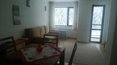 a living room with a table and chairs and two windows at Vadjo Apartments in Complex Stenata Pamporovo in Pamporovo