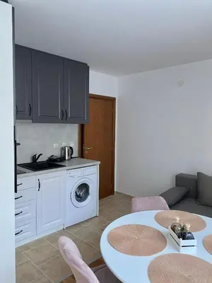 a living room with a table and a kitchen with a washing machine at Pirin Sense apartment A11 in Bansko