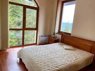 a bedroom with a bed and two large windows at Cedar Heights Cozy Apartments in Pamporovo