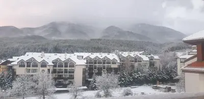 a building covered in snow with mountains in the background at One Bedroom Apartment Pirin Lodge in Bansko