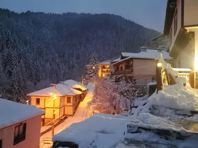a snowy street in a town with snow covered buildings at Майоровата къща in Shiroka Lŭka