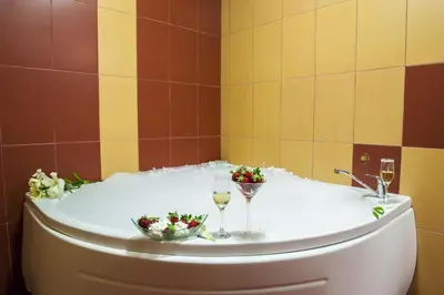a bath tub with two glasses of champagne and flowers at Хотел Дикас in Smolyan