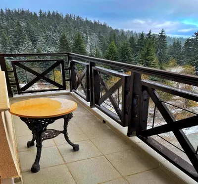 a table on a balcony with a view of a forest at LHApartment! in Pamporovo