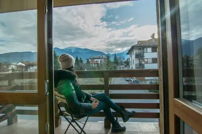 a man sitting in a chair on a balcony looking out a window at Banderitsa Apartment 3 in Bansko