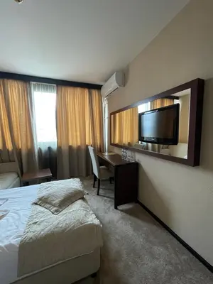 a hotel room with a bed and a desk and a television at Хотел Ботевград in Botevgrad