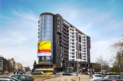 a tall building with cars parked in a parking lot at Green Hills Plovdiv close to Medical University in Plovdiv