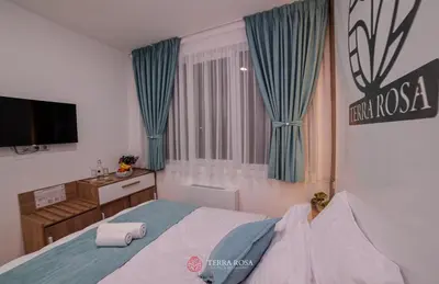 a bedroom with a bed with blue curtains and a television at Хотел Терра Роза in Karlovo