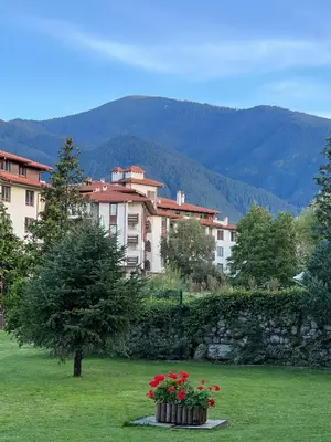a building with flowers in a field with a stone wall at MidnightBlue Apartment in Bansko