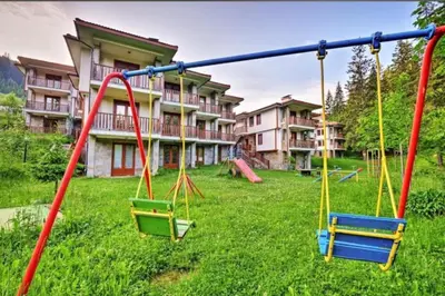 a playground with swings in front of a building at Aparthotel Raikov Ski Lodge in Pamporovo
