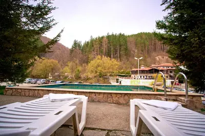 two white benches sitting next to a swimming pool at Вълеви Къщи in Chiflik