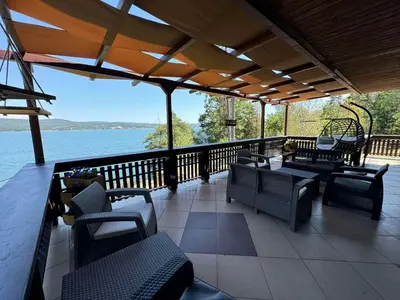 a porch with chairs and tables and a view of the water at Villa Iskar Lake Residence by BookVillaBG in Shtarkelovo Gnezdo