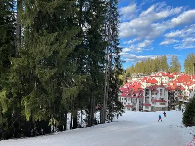 a group of people skiing in the snow in front of a resort at The Castle Mountain Apartments in Pamporovo