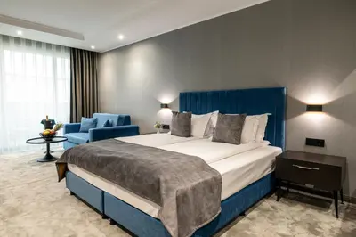 a hotel room with a large bed and a blue chair at Empire Balneo & Spa Hotel in Hisarya