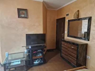 a living room with a television and a dresser with a mirror at Хотел-ресторант Астория in Pazardzhik