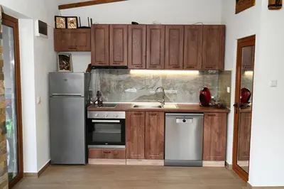 a kitchen with wooden cabinets and stainless steel appliances at Стаи за гости Ингилизовата къща in Padala