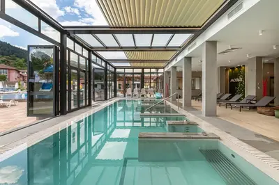 an indoor swimming pool with blue water and glass walls at Парк Хотел Модър in Devin