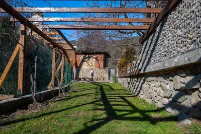 a stone wall with a wooden roof and a fence at Къща за гости Приказка in Klisura