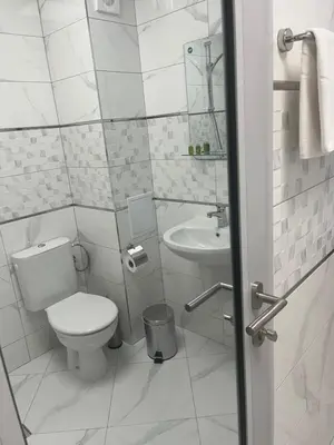 a white bathroom with a toilet and a sink at Хотел Лилия in Rudozem