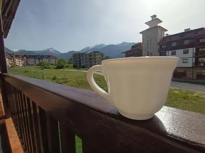 a white coffee cup sitting on a rail on a balcony at Студио в хотел Мария Антоанета in Bansko