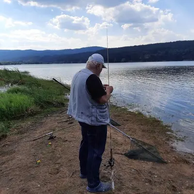a man standing on the shore of a lake holding a fishing pole at Zodiac House in Samokov