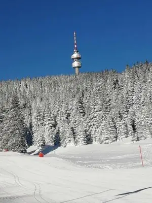 a snow covered hill with a clock tower on a mountain at Апартамент за гости 2Б14 Grand Monastiry in Pamporovo