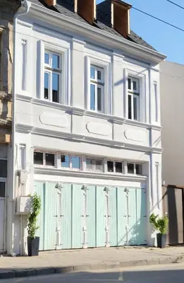 a white house with a green garage door at La Maison des Fleurs FREE PARKING in Pazardzhik