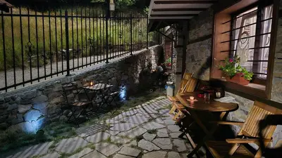 a patio with tables and chairs next to a stone wall at Nachovata Guest House Stoykite, near Pamporovo in Vodata