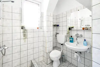 a white tiled bathroom with a toilet and a sink at Creative 70s-Inspired Stay Center Parking in Sofia