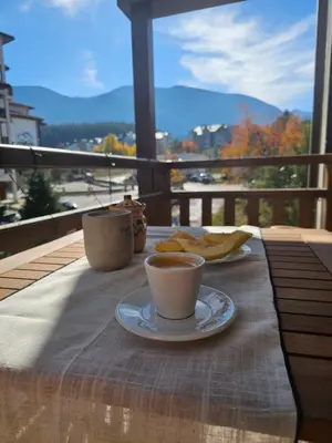 a table with a cup of coffee and chips on a balcony at Ski In Out Aparthotel Kosara in Bansko