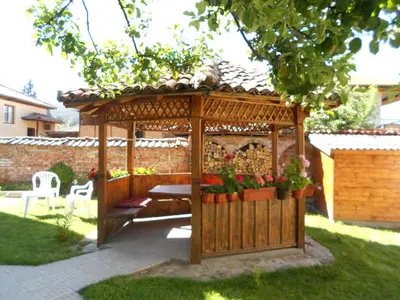 a wooden gazebo with a table and flowers at Guest House Tsenovi in Koprivshtitsa