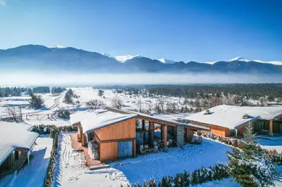a house in the snow with mountains in the background at Pirin Golf Villa Relax in Razlog
