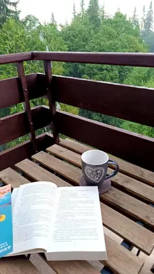 an open book and a cup of coffee on a wooden bench at Апартамент за гости в Пампорово in Pamporovo