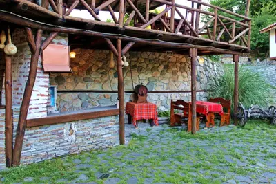 a woman sitting at a table in front of a house at Melnik Pyramids Guesthouse in Zlatkov Chiflik