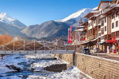 a bridge over a river in a town with snowy mountains at Host2U Slope-Side Home by the Gondola in Bansko